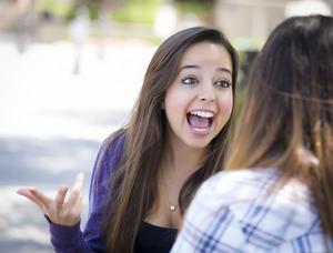 Attractive Expressive Young Mixed Race Female Student Sitting and Talking with Girlfriend Outside on Bench.